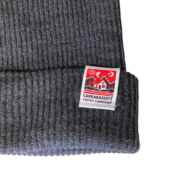 Close-up detail photo of square Carrabassett Coffee Company logo tag on light gray waffle knit beanie hat.