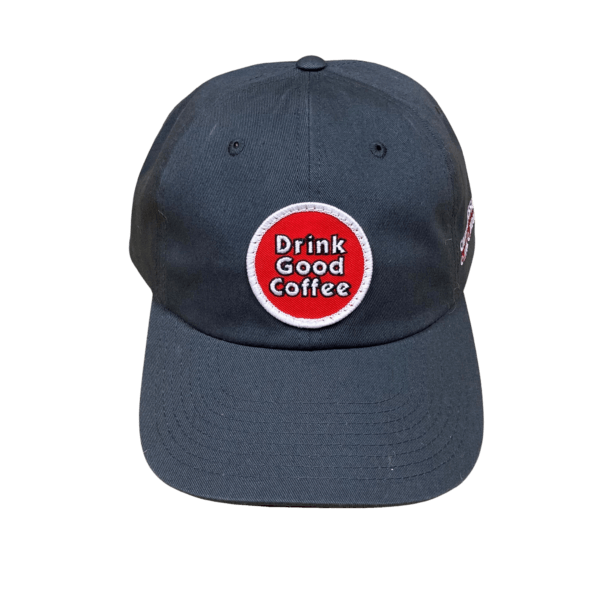 Straight-on front view of the charcoal gray unstructured baseball hat with curved brim. This hat features a circle embroidered patch in red with a white border. Text on the patch reads; Drink Good Coffee in white outlined in black.