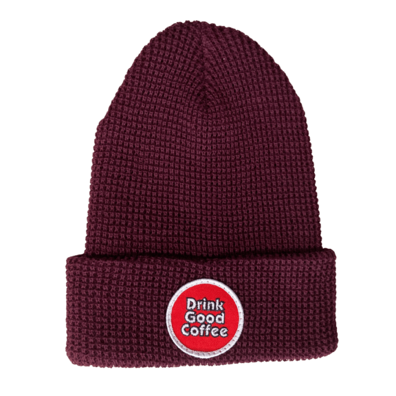Maroon waffle knit beanie winter hat with folded brim and round, red, logo patch embellishment. The patch reads: "Drink Good Coffee" in white.