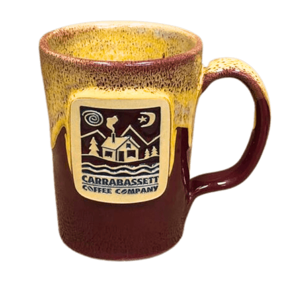 Photograph of burgundy and sand colored coffee mug. The yellowish, sandy color is on the top and drips down to about halfway. The front of the coffee cup has an imprinted embellishment of our house logo with the words: Carrabassett Coffee Company.