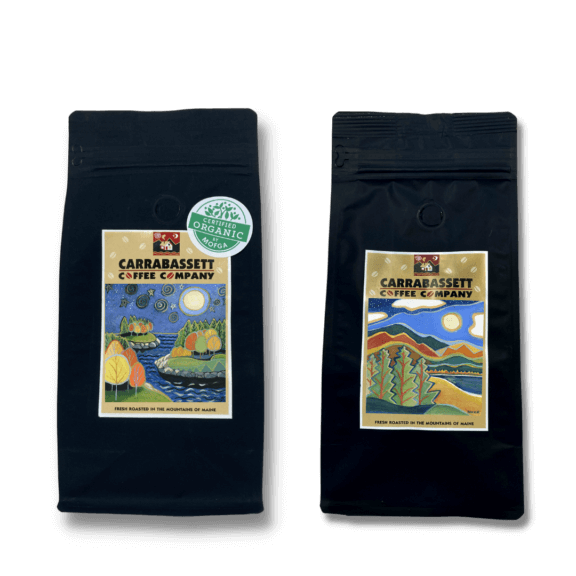 Two black 12-oz bags of Carrabassett coffee featuring generic artwork on the Carrabassett Coffee background to represent the variation of the coffee of the month club.