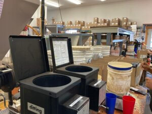 a close-up view of our production line, with coffee grinders in the foreground, scales, and buckets of coffee, and boxes ready to be shipped in the background. 